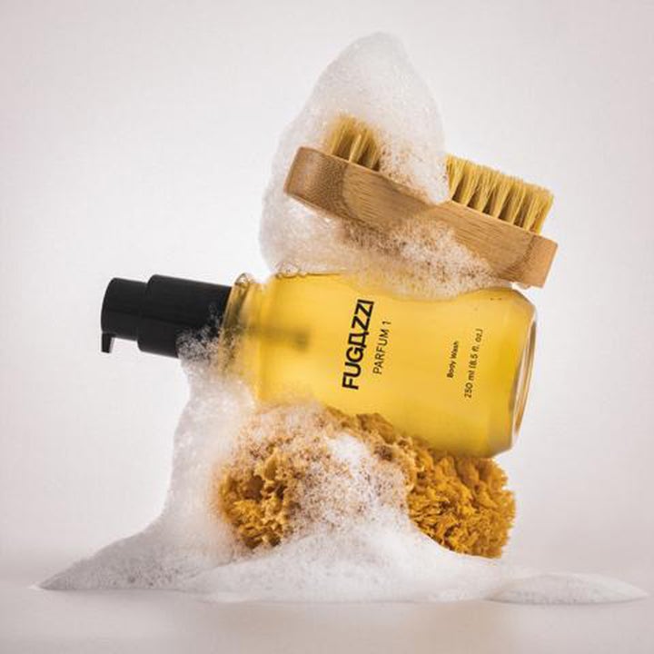 Fugazzi Parfum 1 Body Wash 250 ml dusjsåpe i pumpeflaske omgitt av hvitt skum, natursvamp og trebørste