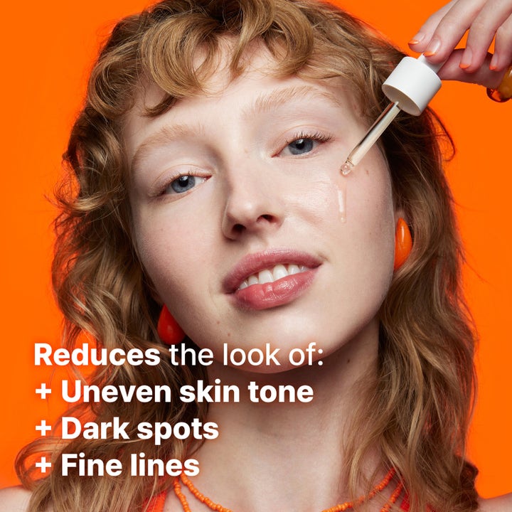Dr.Jart+ Brightamin Brightening Serum Ampoule 8,08 g mot mørke flekker påført på kinnet mot oransje bakgrunn.