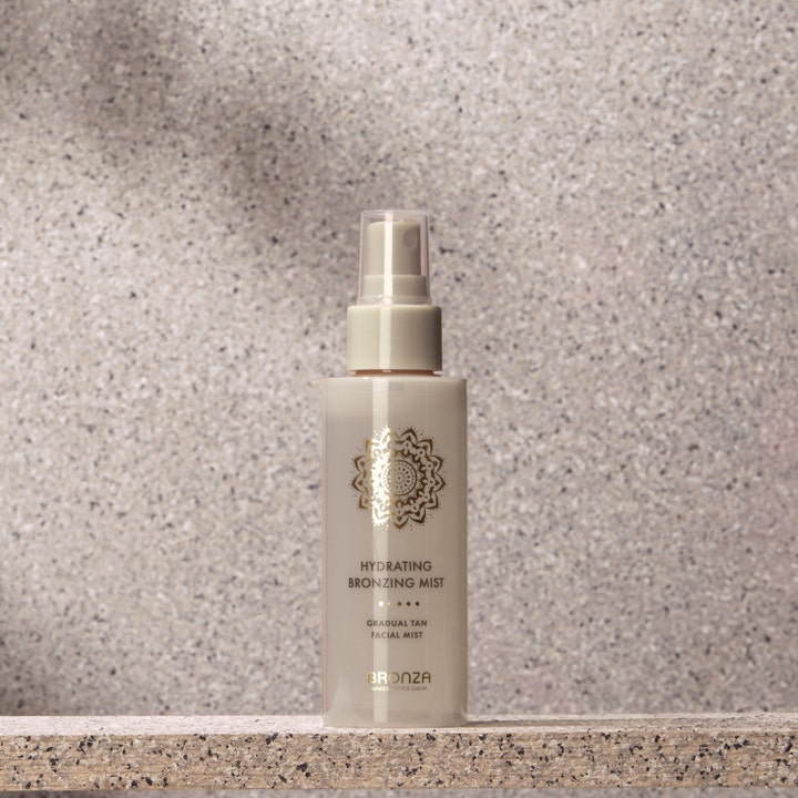 Bronza Hydrating Bronzing Mist Coconut 100 ml fuktighetsgivende selvbruning i beige sprayflaske mot steinbakgrunn