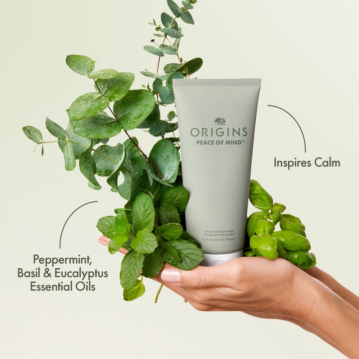 Origins Peace Of Mind 200 ml eksfolierende kroppsskrubb i grå tube omgitt av beroligende eukalyptus, mynte og basilikum