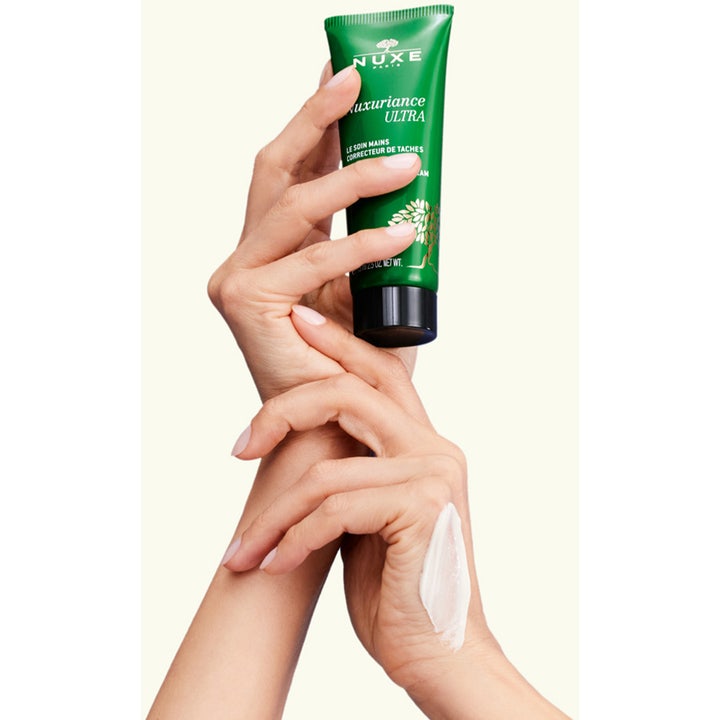 Nuxe Nuxuriance Ultra Hand Cream 90 g fuktighetsgivende håndkrem med hvit tekstur på hendene ved siden av grønn tube.