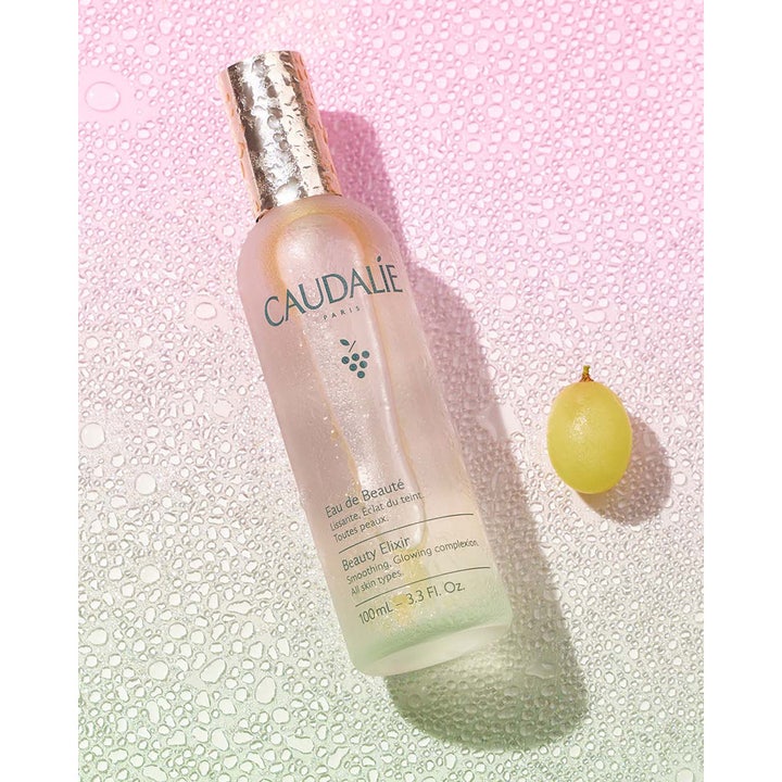 Caudalie Beauty Elixir 100 ml glødgivende toner i frostet glassflaske med gullkork ved siden av en grønn drue