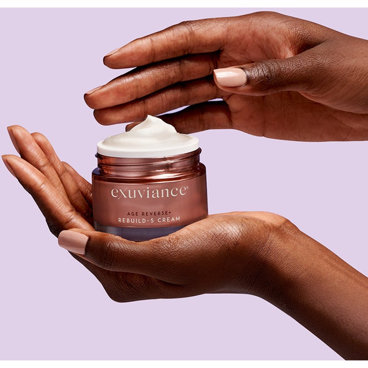 Exuviance Age Reverse + Rebuild-5 Cream 50 ml ansiktskrem i krukke holdt i hendene med synlig hvit tekstur.
