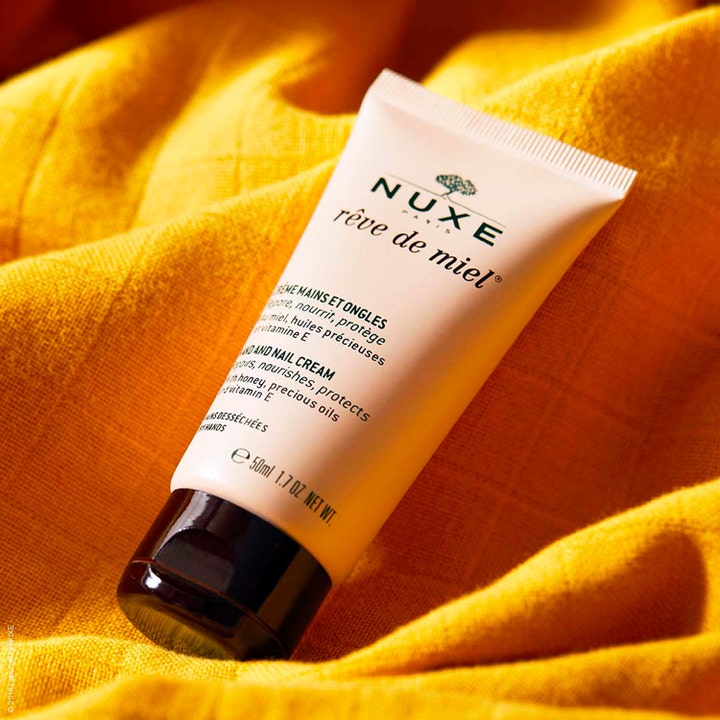 Nuxe Rêve de Miel Hand and Nail Cream 50 ml reparerende håndkrem i beige tube plassert på gult strukturert stoff.