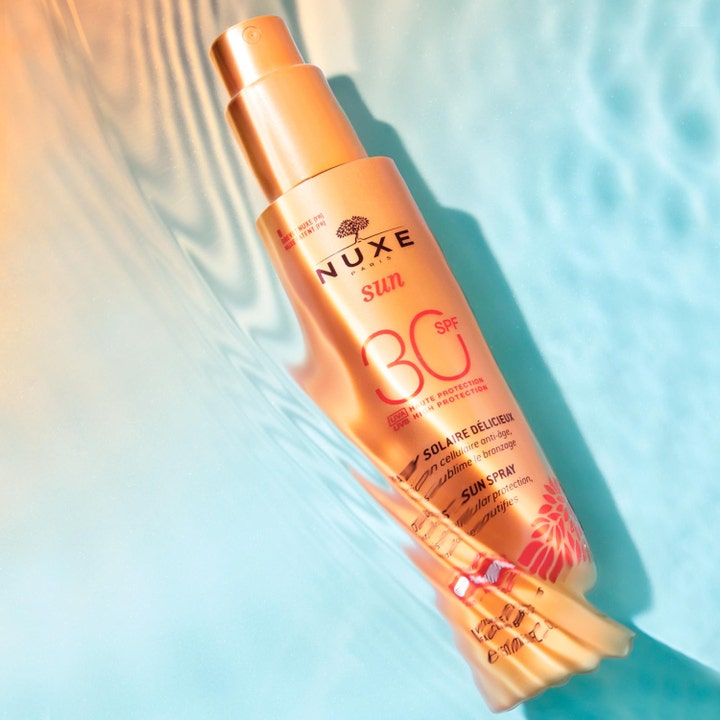 Nuxe Sun Spray SPF30 184 g solkrem for ansikt i bronsefarget sprayflaske som ligger i bølgende blått vann