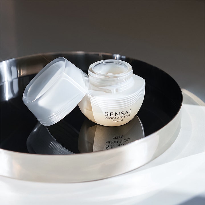 Sensai Absolute Silk Cream 40 ml ansiktskrem i åpen perlehvit krukke på et sølvfat som viser konsistensen