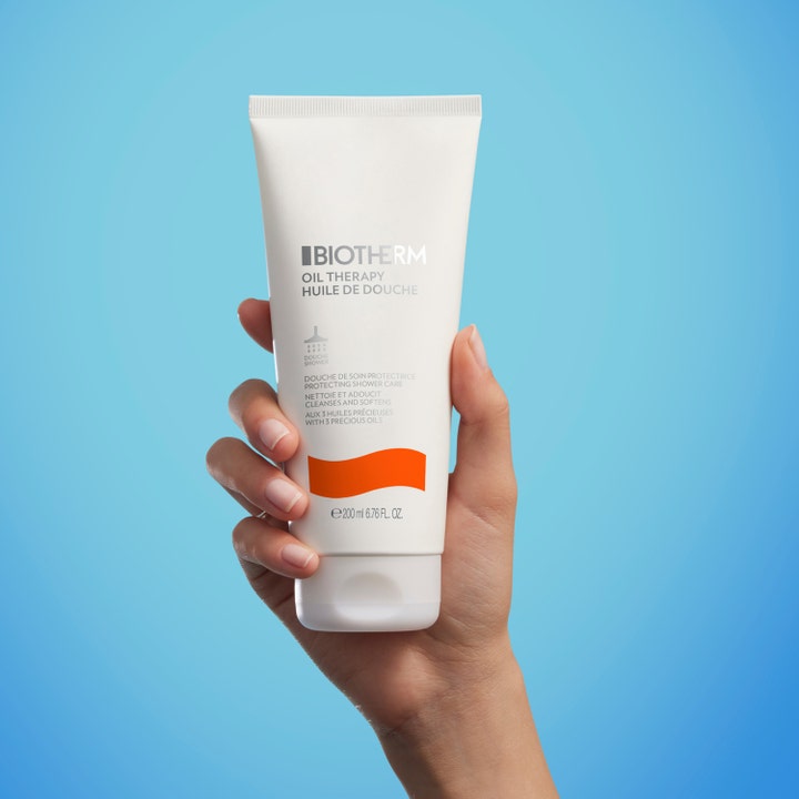 Biotherm Oil Therapy 200 ml fuktighetsgivende dusjolje i hvit tube med oransje detalj holdes av en hånd