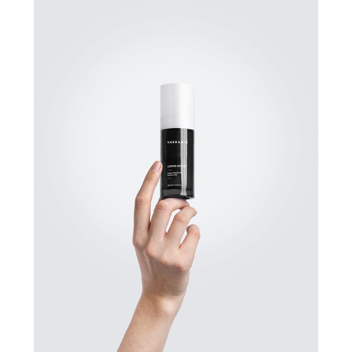 Niche Beauty Lab Theramid Copper Peptide 30 ml antialdringsserum i svart flaske med hvit kork holdt av en hånd.