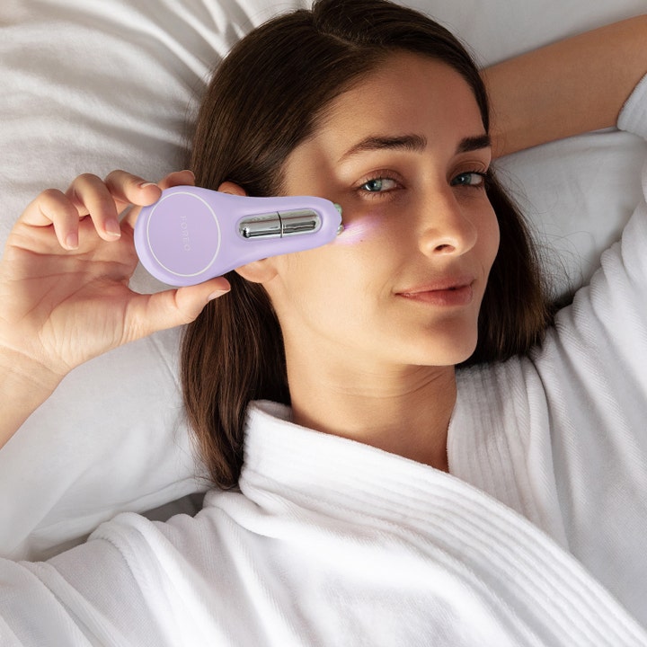 FOREO BEAR 2 eyes & lips 1 stk mikrostrømapparat kvinne i hvit badekåpe behandler huden under øynene for et løft