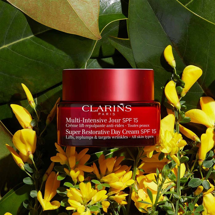 Clarins Super Restorative Day Cream 50 ml dagkrem med SPF 15 i rød krukke omgitt av grønne blader og gule blomster.