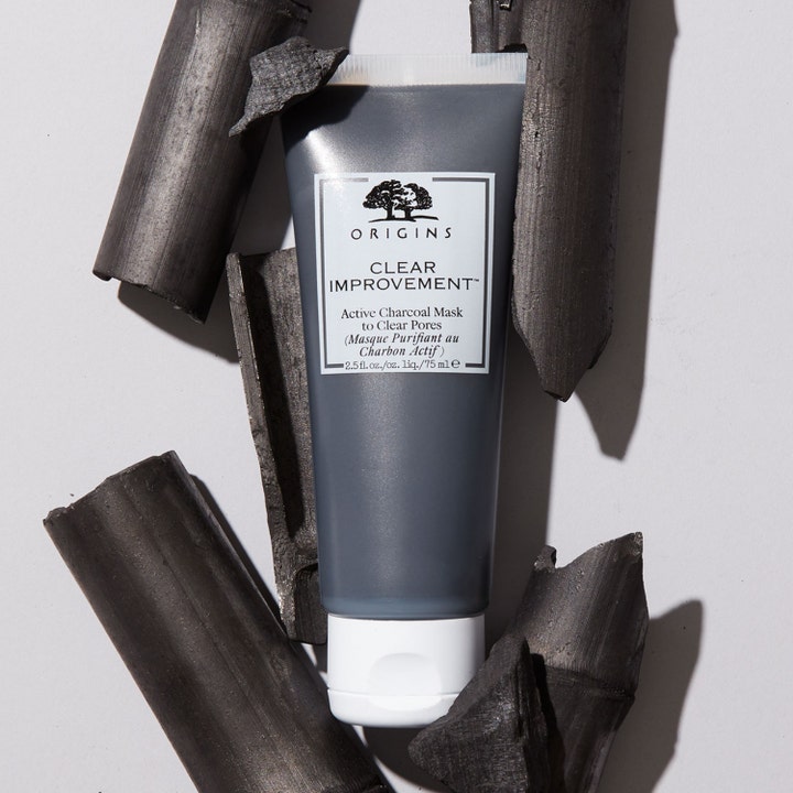 Origins Clear Improvement Active Charcoal Mask 75 ml rensende ansiktsmaske i grå tube omgitt av biter med aktivt kull