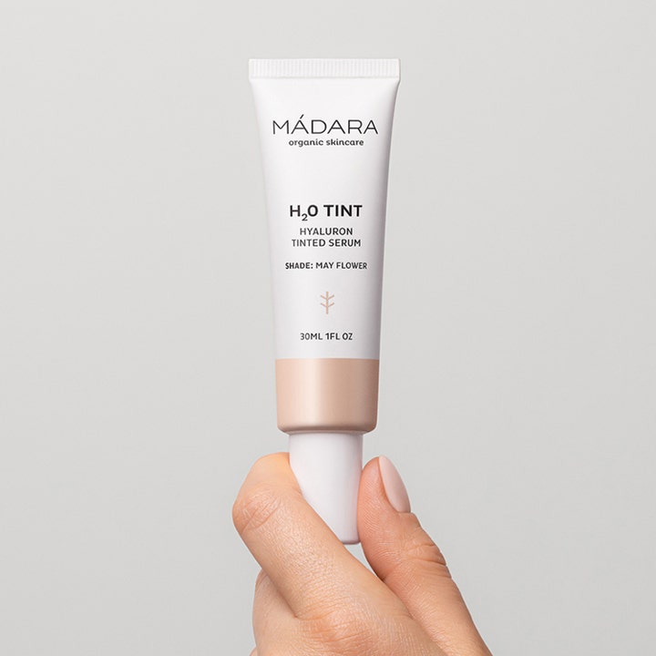 MÁDARA H2O Tint Hyaluron Tinted Serum 30 ml May Flower fuktighetsgivende serum i hvit tube holdt i hånden
