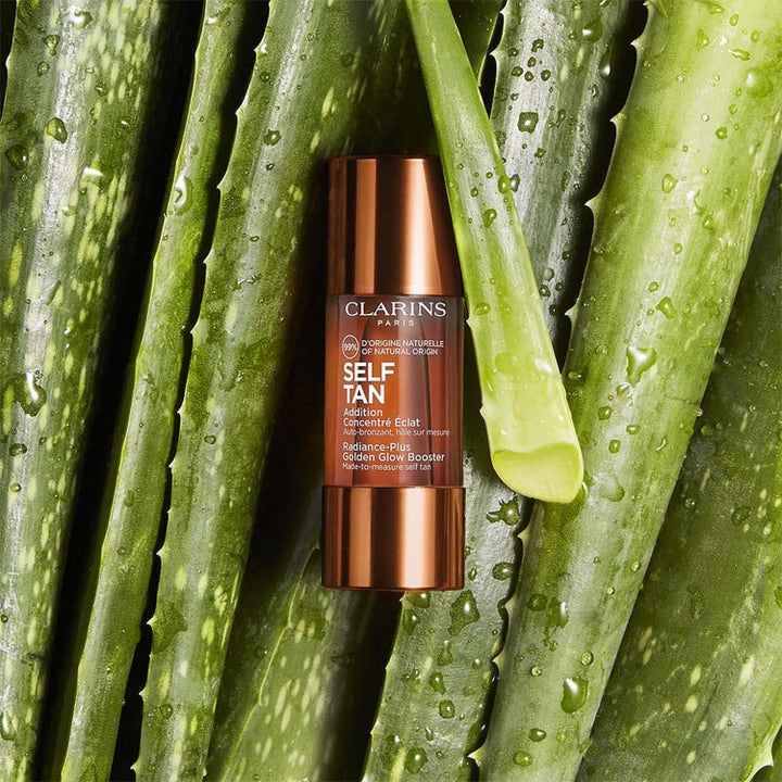 Clarins Golden Glow Booster selvbruningsdråper i bronseflaske som gir glød omgitt av friske aloe vera-blader.