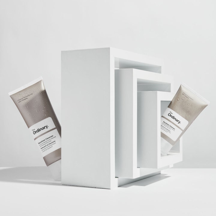 The Ordinary Squalane Cleanser 50 ml ansiktsrengjøring med vanndråper på tubene ved hvite geometriske former