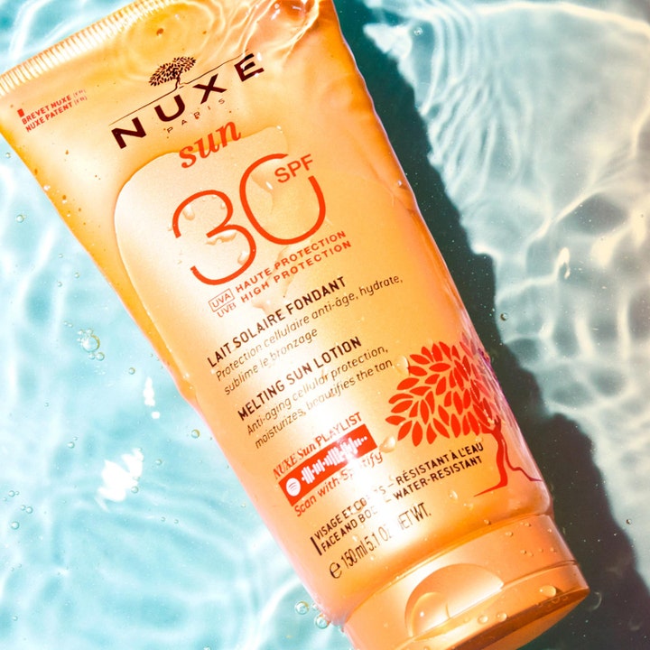 Nuxe Sun Delicious Lotion 150 ml solbeskyttelse SPF30 i oransje tube omgitt av klart, bølgende vann.