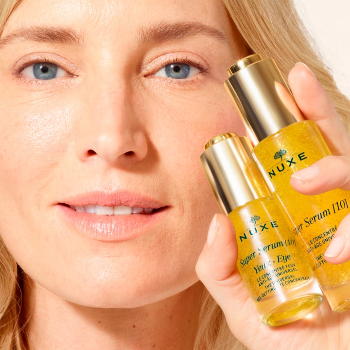 Nuxe Super Serum [10] Eye 15 ml anti-age øyeserum i gullflaske som holdes av en kvinne for glødende hud.