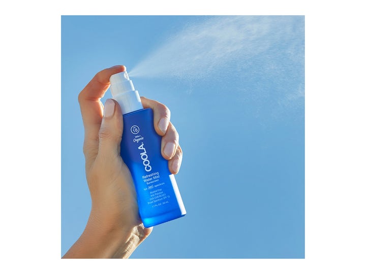 COOLA Refreshing Water Mist 50 ml fuktighetsgivende ansiktsspray i blå flaske som sprayes mot en blå himmel