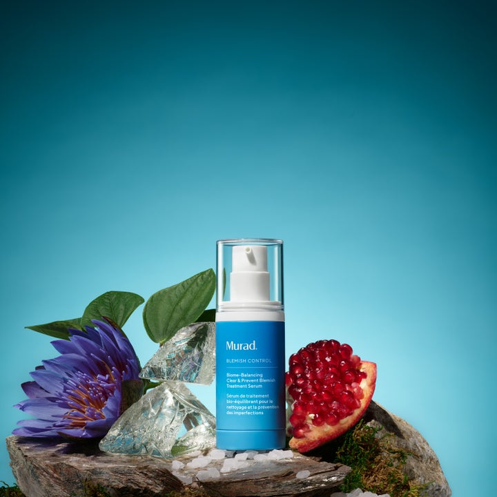 Murad Biome-Balancing Clear & Prevent Blemish Treatment Serum 30 ml står på en stein ved granateple og en lilla blomst.