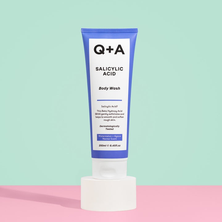 Q+A Salicylic Acid Body Wash 250 ml eksfolierer og mykgjør huden i blå og hvit tube på hvit sokkel.