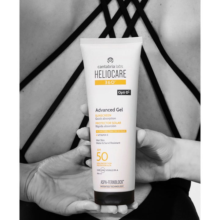Heliocare Advanced Gel 250 ml solkrem med SPF 50 og Vitamin E i hvit tube holdt mot en bar rygg.