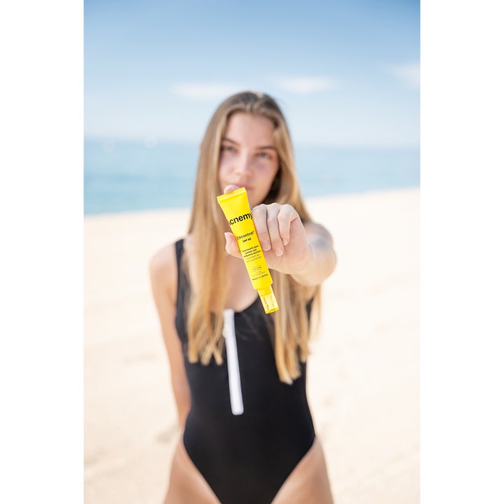 Niche Beauty Lab Acnemy Zitcontrol 40 ml SPF 50 dagkrem i gul tube holdt av en kvinne på en solfylt strand