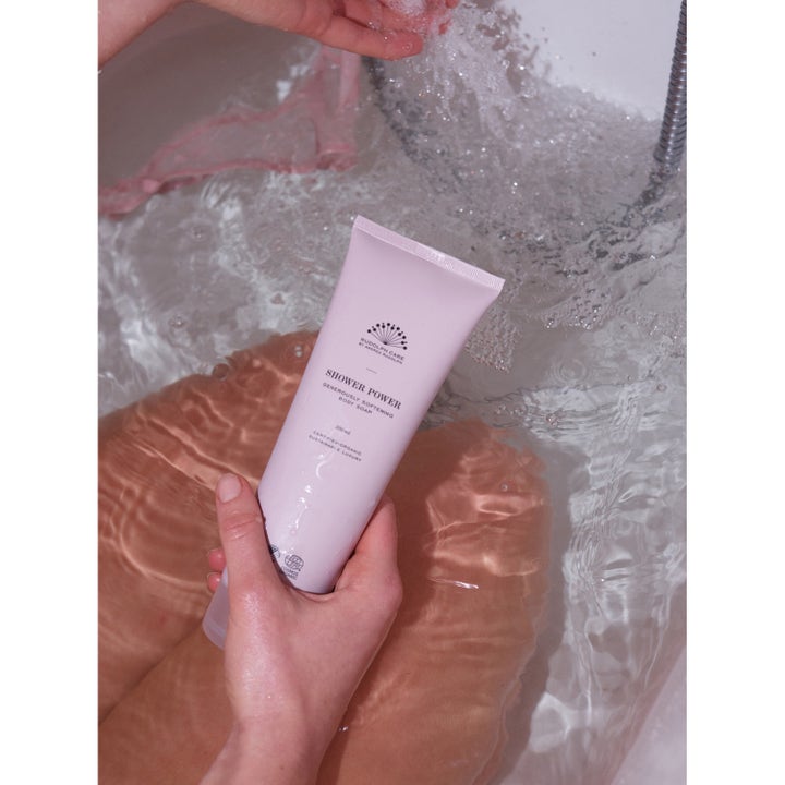 Rudolph Care Acai Shower Power 250 ml mykgjørende dusjsåpe i rosa tube som holdes under vann i et badekar