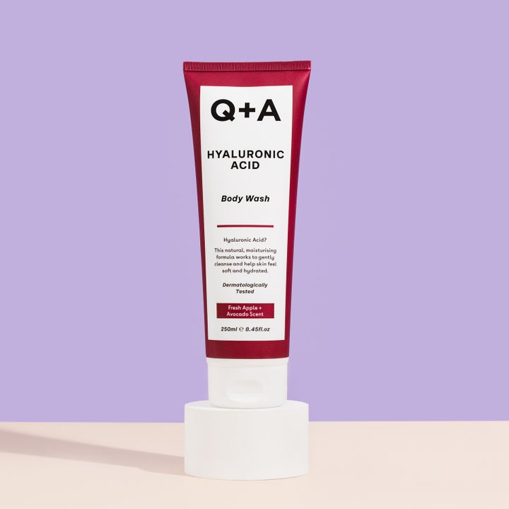 Q+A Hyaluronic Acid Body Wash 250 ml fuktighetsgivende dusjsåpe i rød tube stående på en hvit sokkel.