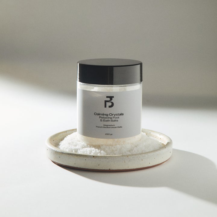 Bodyologist Calming Crystals 250 g badesalt gir avslapning i krukke med sort lokk på et fat med hvite saltkrystaller.