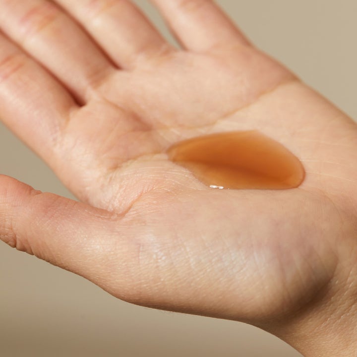 Hyggee Natural Repair Serum 30 ml reparerende serum med en ravfarget flytende tekstur i en håndflate.