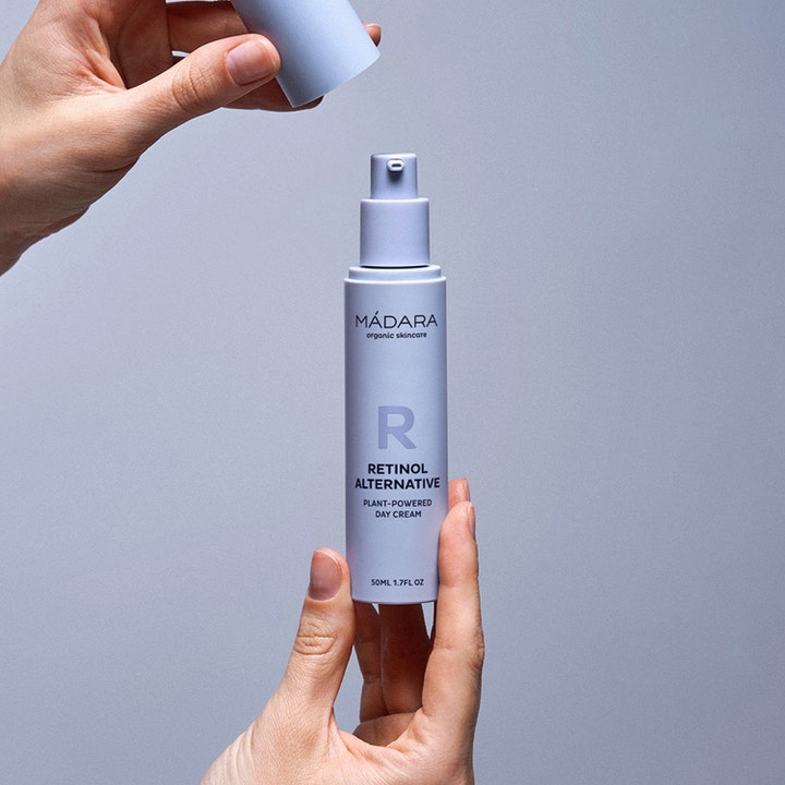 MÁDARA RETINOL ALTERNATIVE 50 ml dagkrem i lilla pumpeflaske som holdes opp av hender mot nøytral bakgrunn
