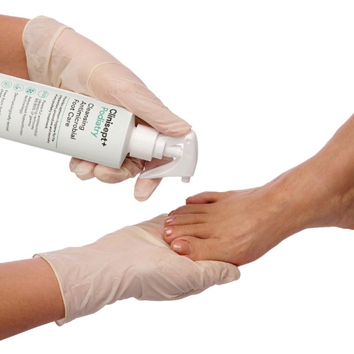 Clinisept+ Podiatry Foot Care Spray 250 ml antimikrobiell fotpleie og behandling som sprayes på en fot med hansker.