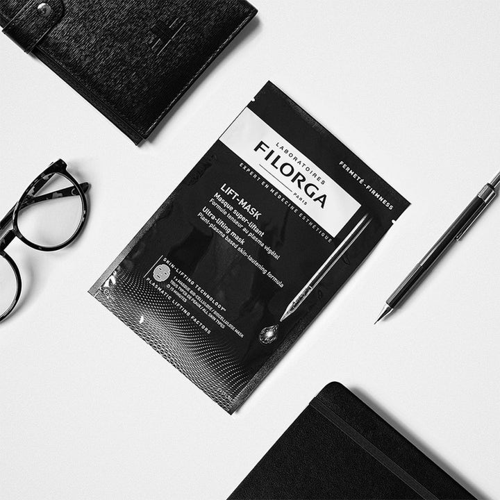 Filorga Lifting & Firming Set oppstrammende sheet mask i svart sachet ved siden av sorte briller og en penn.