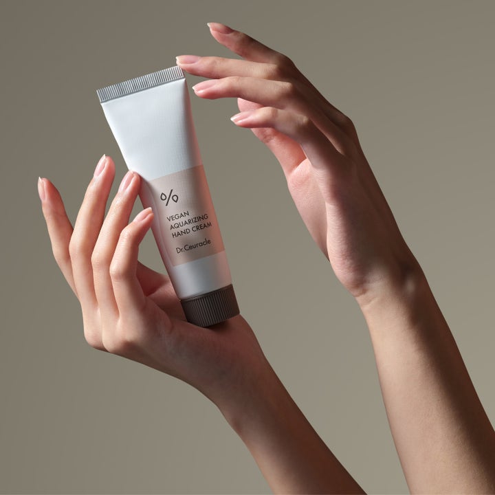 Dr. Ceuracle Vegan Aquarizing Hand Cream 50 ml vegansk håndkrem i hvit tube med ferskenfarget etikett holdt av hender.