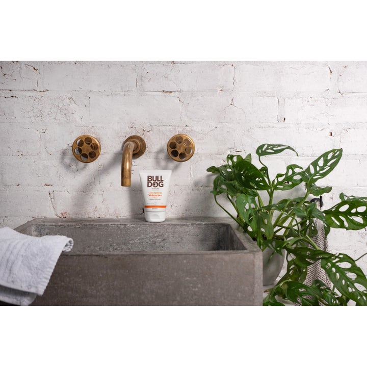 Bulldog Energising Moisturiser 100 ml ansiktskrem som gir glød i hvit tube ved en messingkran og grønn plante