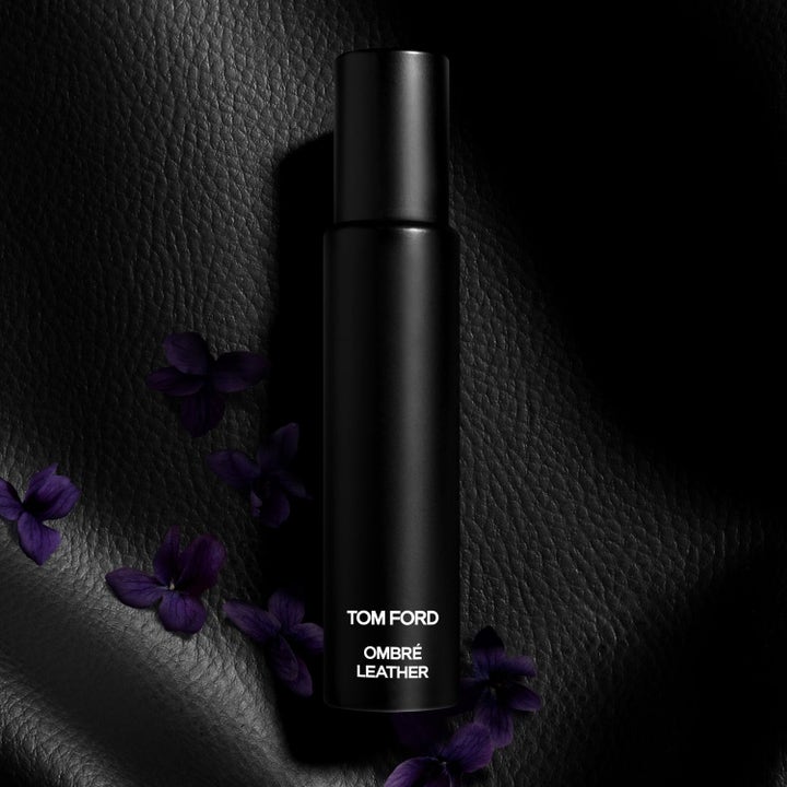 Tom Ford Ombré Leather duft i matt svart sprayflaske plassert på mørkt skinn med lilla blomsterblader