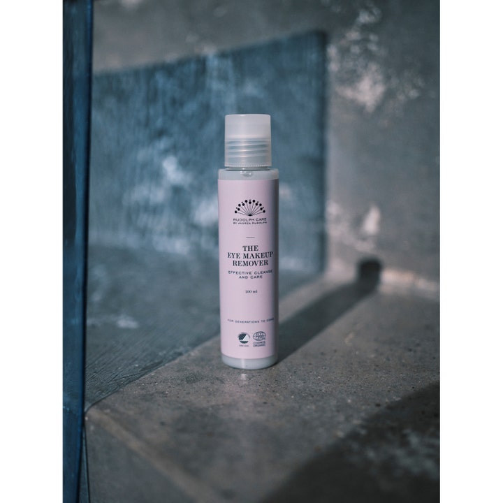 Rudolph Care The Eye Makeup Remover 100 ml pleiende sminkefjerner i rosa flaske på en steintrapp