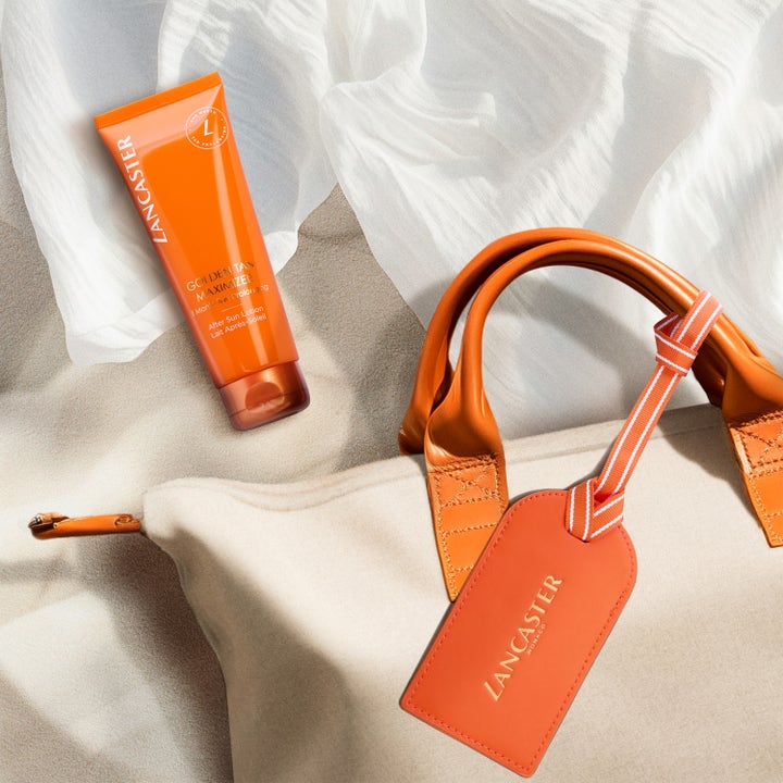 Lancaster Golden Tan Maximizer After Sun Lotion 125 ml i oransje tube ved siden av en strandveske på sand.