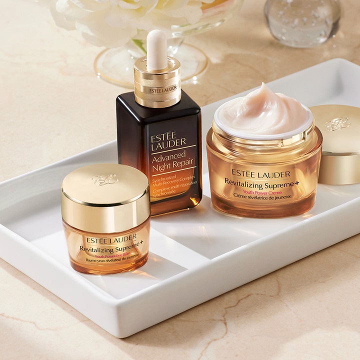 Estée Lauder Revitalizing Supreme + Youth Power Eye Balm 15 ml øyekrem i gullkrukke på et hvitt brett med ansiktskrem