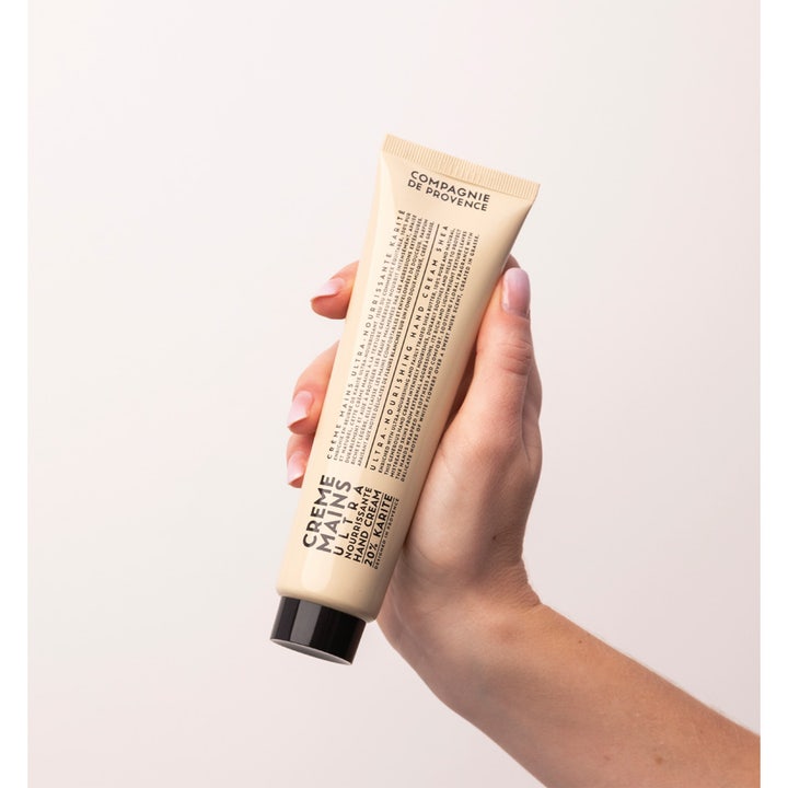 Compagnie de Provence Hand Cream Shea Butter 100 ml nærende håndkrem i beige tube som holdes av en hånd med lyse negler