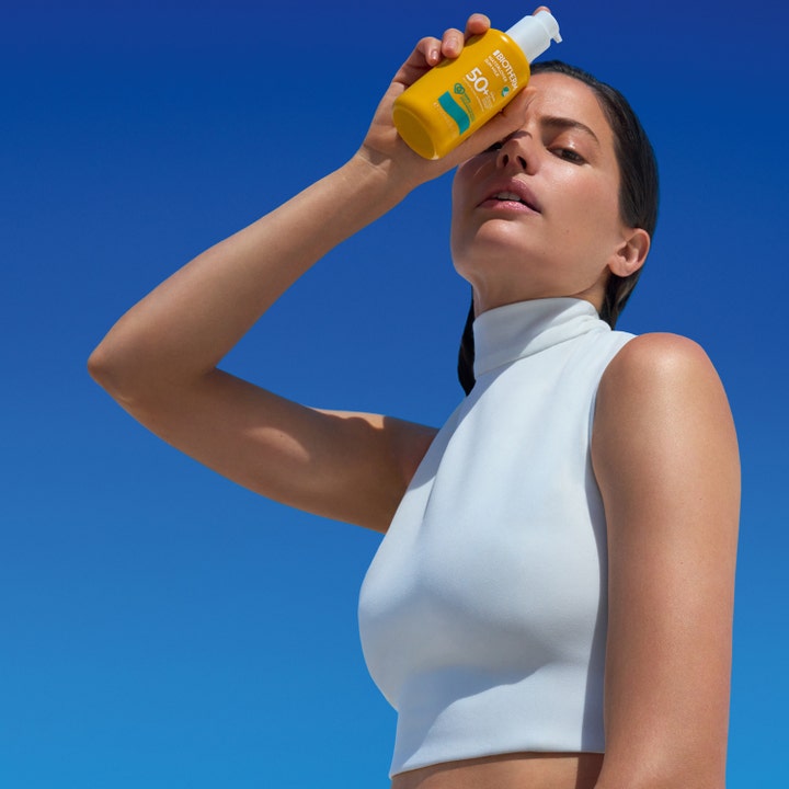 Biotherm Waterlover Sun Milk 200 ml beskyttende solkrem i gul flaske holdes av en kvinne mot en klar blå himmel