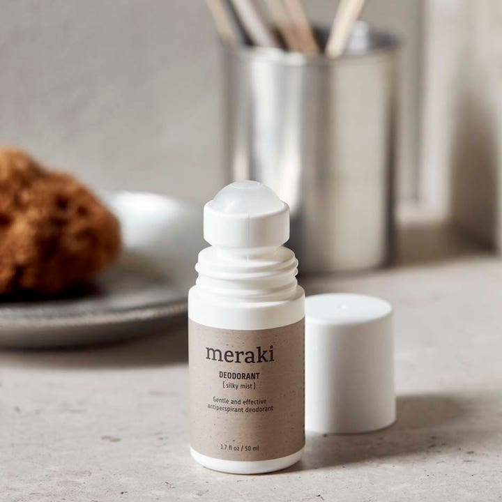 Meraki Silky Mist Deodorant 50 ml gir effektiv beskyttelse i en hvit roll-on flaske vist åpen i et spa-inspirert miljø