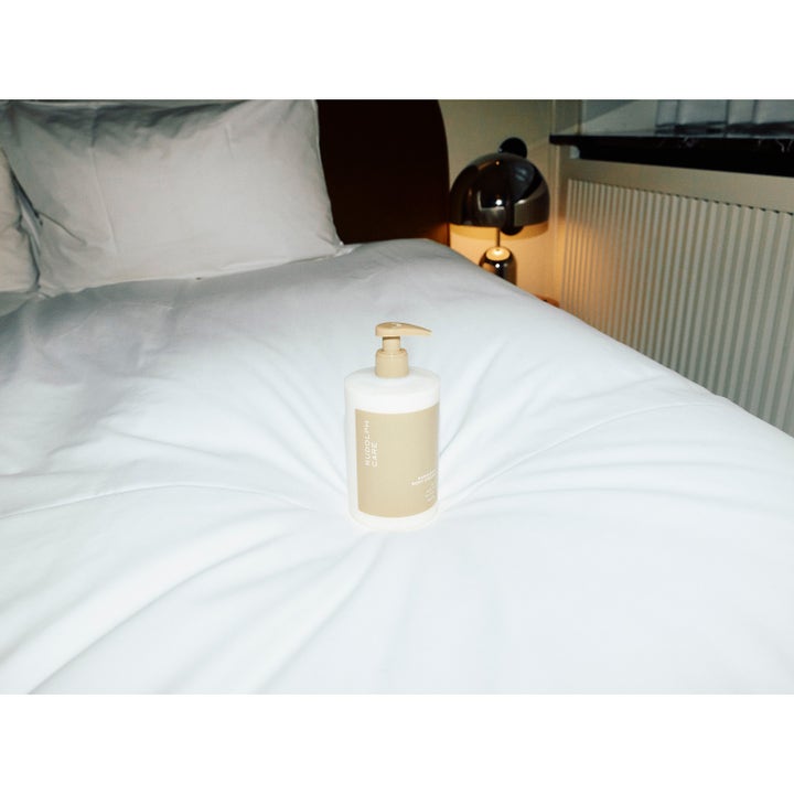 Rudolph Care Hand And Body Cream 500 ml pleiende bodylotion i pumpeflaske på en hvit oppredd seng