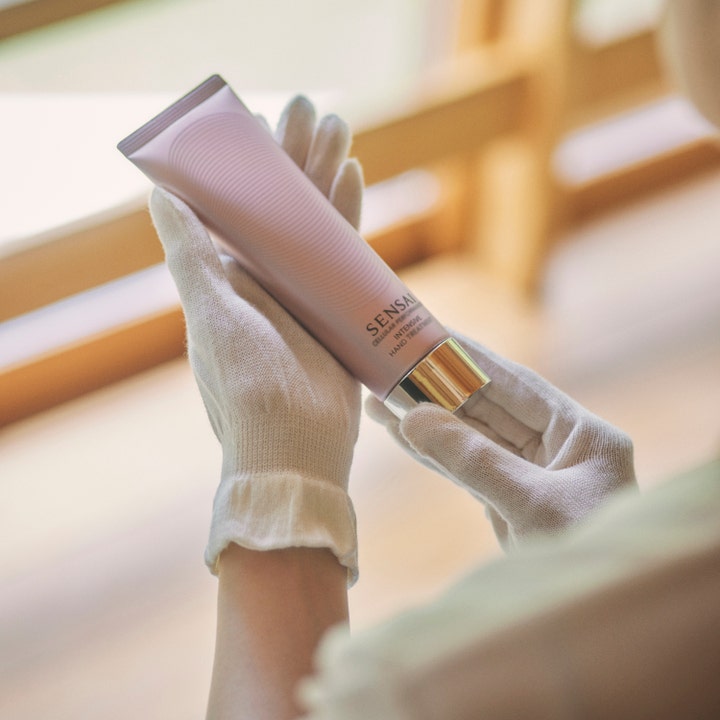 Sensai Cellular Performance Intensive Hand Treatment 100 ml pleiende håndkrem i tube holdt av hender med hvite bomullshansker
