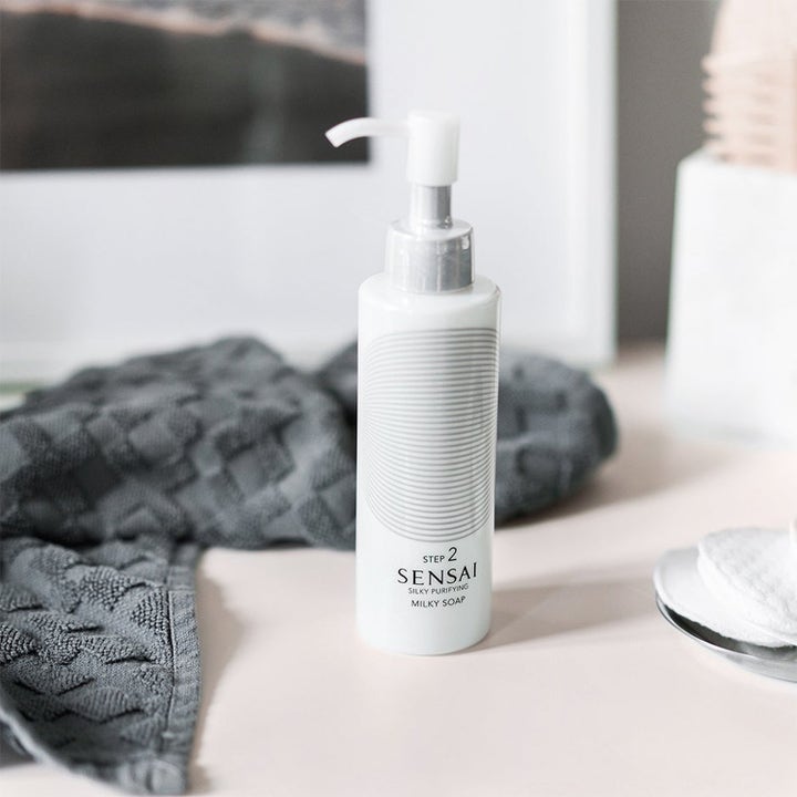Sensai Silky Purifying Milky Soap 150 ml ansiktsrens i hvit pumpeflaske plassert ved en grå vaskeklut