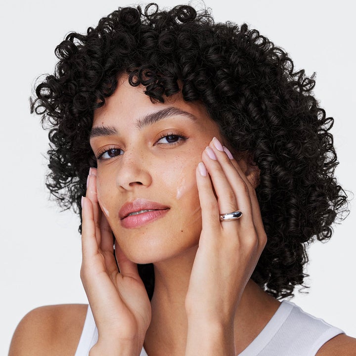 Clinique Retinol Intro retinol-behandling kvinne med mørke krøller som påfører en lett krem i ansiktet.