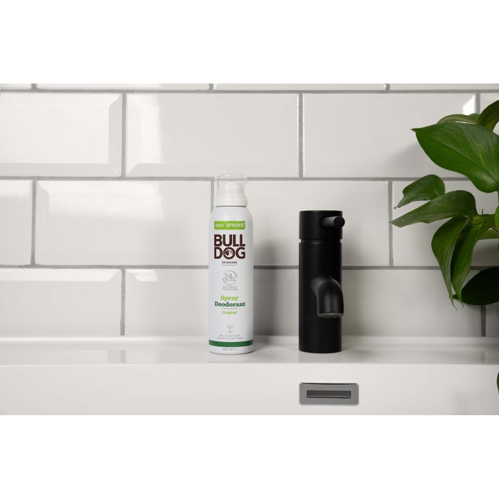 Bulldog Spray Deodorant Original 125 ml på en baderomshylle ved siden av en sort kran og grønne blader