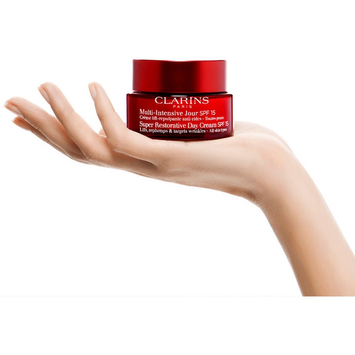 Clarins Super Restorative Day Cream 50 ml dagkrem med SPF 15 som motvirker rynker i en rød glasskrukke holdt i en hånd