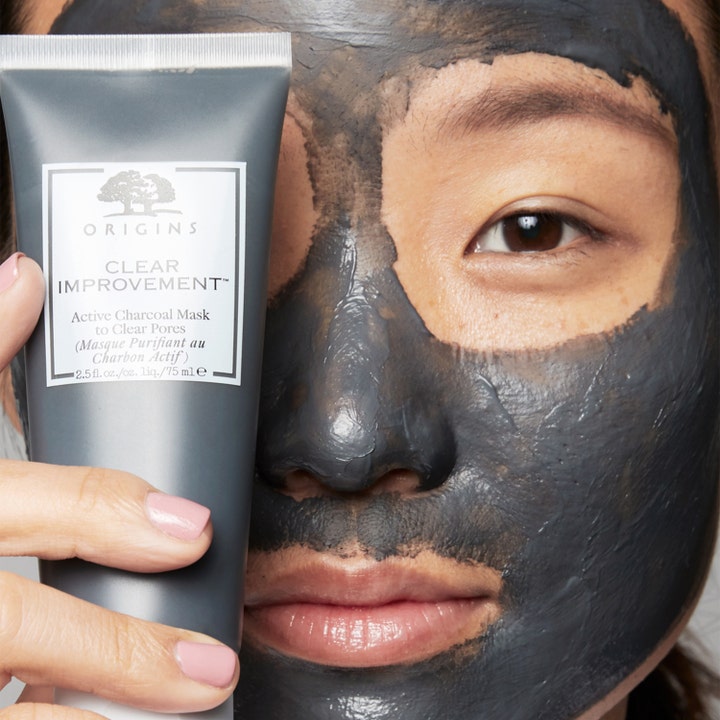 Origins Clear Improvement Active Charcoal Mask 75 ml rensende kullmaske vist påført i ansiktet ved siden av tuben.