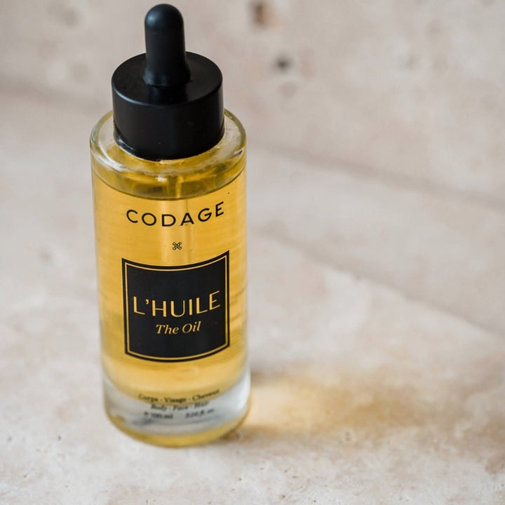 Codage Paris The Oil 100 ml nærende kroppsolje i en klar glassflaske med svart pipette på lys stein.