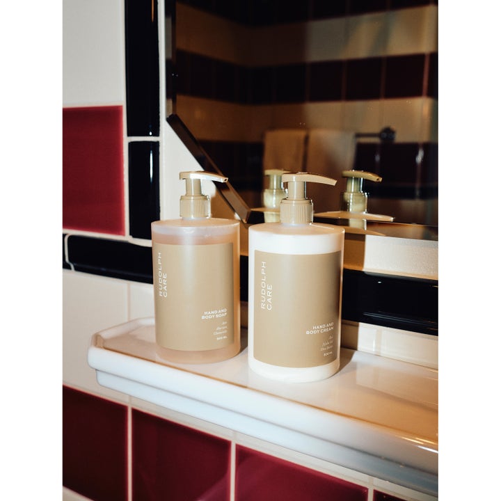 Rudolph Care Hand And Body Cream 500 ml pleiende kroppskrem i hvit pumpeflaske på baderomshylle foran et speil.